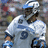 Pixelated static image of a person in a white uniform with blue accents holding a baseball bat, standing in a field.