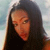 A pixelated close-up of a person with long dark hair wearing a dark top against a light background.