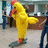 A pixelated image of a person in a yellow chicken costume with red accents standing indoors, next to a blue with black text