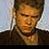 Static pixelated image of a person's face and upper torso in warm tones with dark hair, wearing a dark jacket over a light shirt against a pale background.
