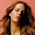 A static pixelated image shows a person with long brown hair against a solid pink background, wearing a light-colored top.