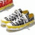 A pair of yellow sneakers with white laces and black-and-white patterned uppers, positioned on a white background with a partial red object visible in the top-left corner.