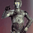 Static pixelated image of a humanoid robot with metallic silver and black coloring, raised arm pose against dark purple background.