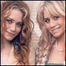 Two women with long wavy hair appear in a split- view, one in a green top with a necklace, the other in a light jacket over blue jeans holding a small object