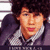 Pixelated image of a person with curly hair wearing a gray jacket over a checkered shirt, with pink text overlays and a small arrow graphic.