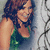 A woman with brown curly hair wears a green sleeveless top and a dark choker necklace, smiling against a light background with dark swirling lines.