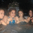 Pixelated image of four people in water with pink text labels on black background.