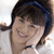 A pixelated close-up of a smiling person with dark hair tied in pigtails, wearing a white top and dark headband, against a light background.