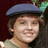 Pixelated close-up of a person wearing a dark blue flat cap and light green shirt against dark background.