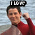 A person in a red and gray wetsuit stands against water, with text changing from 'I LOVE' to 'YOU' across frames.