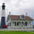 A static pixelated image shows a lighthouse with black and white stripes next to a two-story house with a brown roof and green trim, set against a cloudy sky.