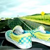 A pair of yellow and blue checkered sneakers on a road with green fields and a yellow sign in the background.