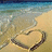 Pixelated beach scene with light blue water, sandy shore, and a heart shape drawn in the sand.