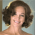 Pixelated close-up of a person with curly brown hair smiling, showing teeth, against a light blue background with a brown vertical element on the left.