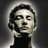 Pixelated grayscale portrait of a person with short dark hair wearing a black top against a gradient background, rendered in low-resolution 256x256 pixels.