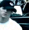 A person wearing a dark cap with a red and white emblem, light-colored shirt, and earrings appears in four showing slight head movement