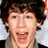Pixelated close-up of a person with dark curly hair, light skin, and an open mouth showing teeth against a blurred background.