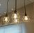 Three hanging light fixtures with warm glowing bulbs suspended by dark cords against a blurred background of neutral tones.