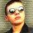 Static pixelated image of a person wearing sunglasses and dark clothing against a striped background.