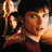 Pixelated image of a person with brown hair holding a flag, wearing a red outfit with a blue collar, against a dark background.