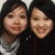 Two people with dark hair pose closely together, one wearing a light-colored top and the other in dark clothing against a neutral background.
