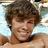 Pixelated image of a person with brown curly hair lying on light blue fabric, next to cyan text reading Mrs. Ryan Sheckler.