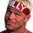 Pixelated static image of a person's face with red and white patterns on the head, set against a plain background.