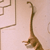 Brown dinosaur with long neck and tail stands on light beige background, partially cropped at left edge.