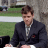 Static 48x48 pixel icon showing a man in formal attire seated outdoors with blurred background elements.