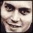 Pixelated close-up of a face with dark eyebrows, eyes looking slightly left, and a wide grin showing teeth.