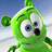 Green cartoon character with large blue eyes and a black mouth, floating against a light blue sky background.