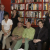 Six people stand in front of a bookshelf filled with books, wearing casual clothing in muted tones.