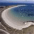 A pixelated beach scene with a curved shoreline, blue water, and sandy foreground under a light blue sky.