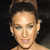 Pixelated close-up of a person's face with light skin tone, dark hair styled upward, and visible ear with small earring against dark background.