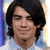 Pixelated portrait of a person with dark shoulder-length hair, light skin, and a neutral expression wearing a light-colored shirt against a blurred background.