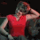 A woman in a red sleeveless top and dark pants performs a sequence of arm movements against a dark background.