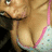 Pixelated close-up of a person's face and upper chest with light skin tone, wearing dark clothing on the left side and pink straps over a white patterned garment.