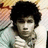 A person with dark curly hair wearing a light-colored striped shirt, positioned against a patterned background.