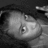 Grayscale pixelated image of a stylized face with large eyes and smooth shading, set against dark background elements.