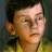 Pixelated close-up of a person with short dark hair wearing a yellow garment against a dark background.
