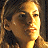 Pixelated close-up of a person's face with light brown hair, wearing a dark top, against a dark background with warm lighting.