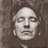 Pixelated grayscale portrait of a person with closed eyes, neutral expression, and visible ear, set against a textured background.