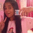 A pixelated static image shows a person with long dark hair wearing a light-colored top, holding an object near their face against a pink-toned background.