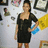 A pixelated static image shows a person in a black dress holding a blue object against a light background with framed items.