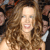 A pixelated close-up of a person with long brown hair, light skin, and a smiling expression, wearing a dark strapless dress with a light-colored shoulder detail.
