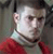 Pixelated static image of a person in red clothing with light-colored hair and visible facial features against a dark background.