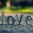 Pixelated image showing the word 'Love' in dark blue letters over a reflective water surface with a blurred background of green and yellow tones.