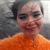 Pixelated image of a person with short light hair wearing an orange shirt against a gray background.