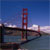 Pixelated static image of a red suspension bridge with vertical towers against a blue sky and water, viewed from a low angle with landmasses on both sides.