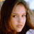 Pixelated close-up of a person with long brown hair against a blurred background, showing partial facial features and clothing details.